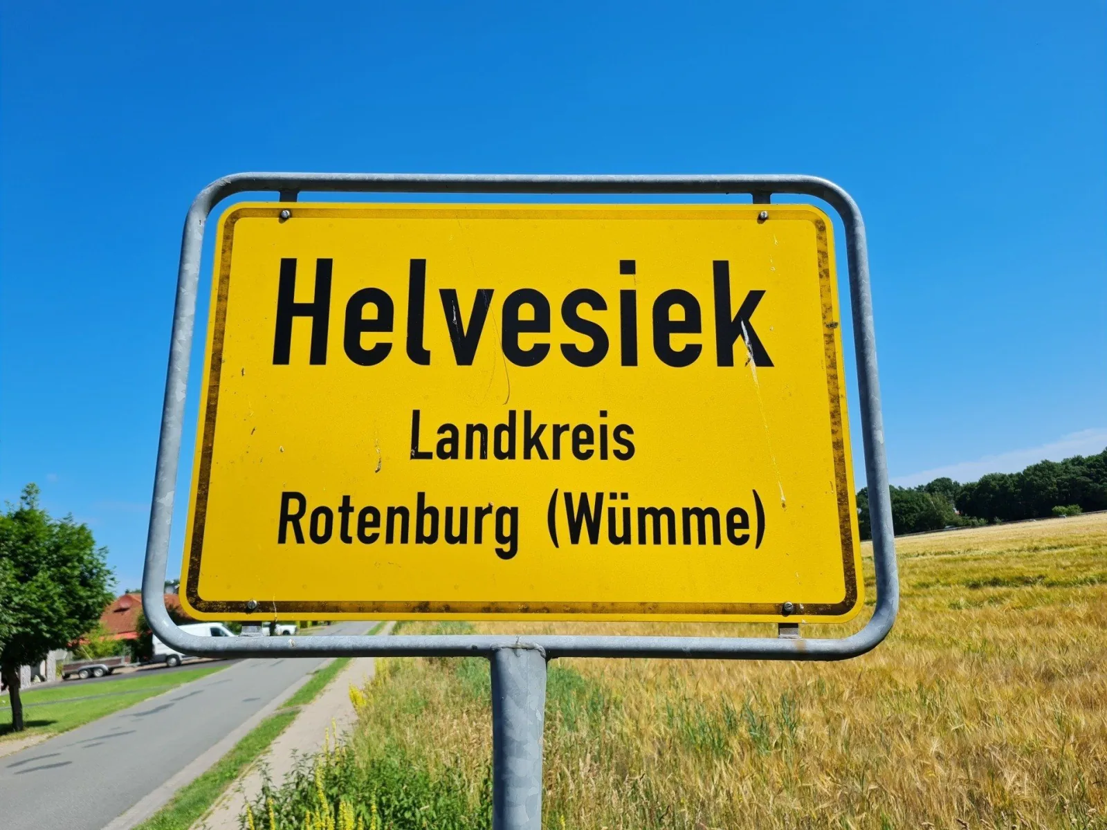 Ortsschild von Helvesiek vor Feldern und blauem Himmel
